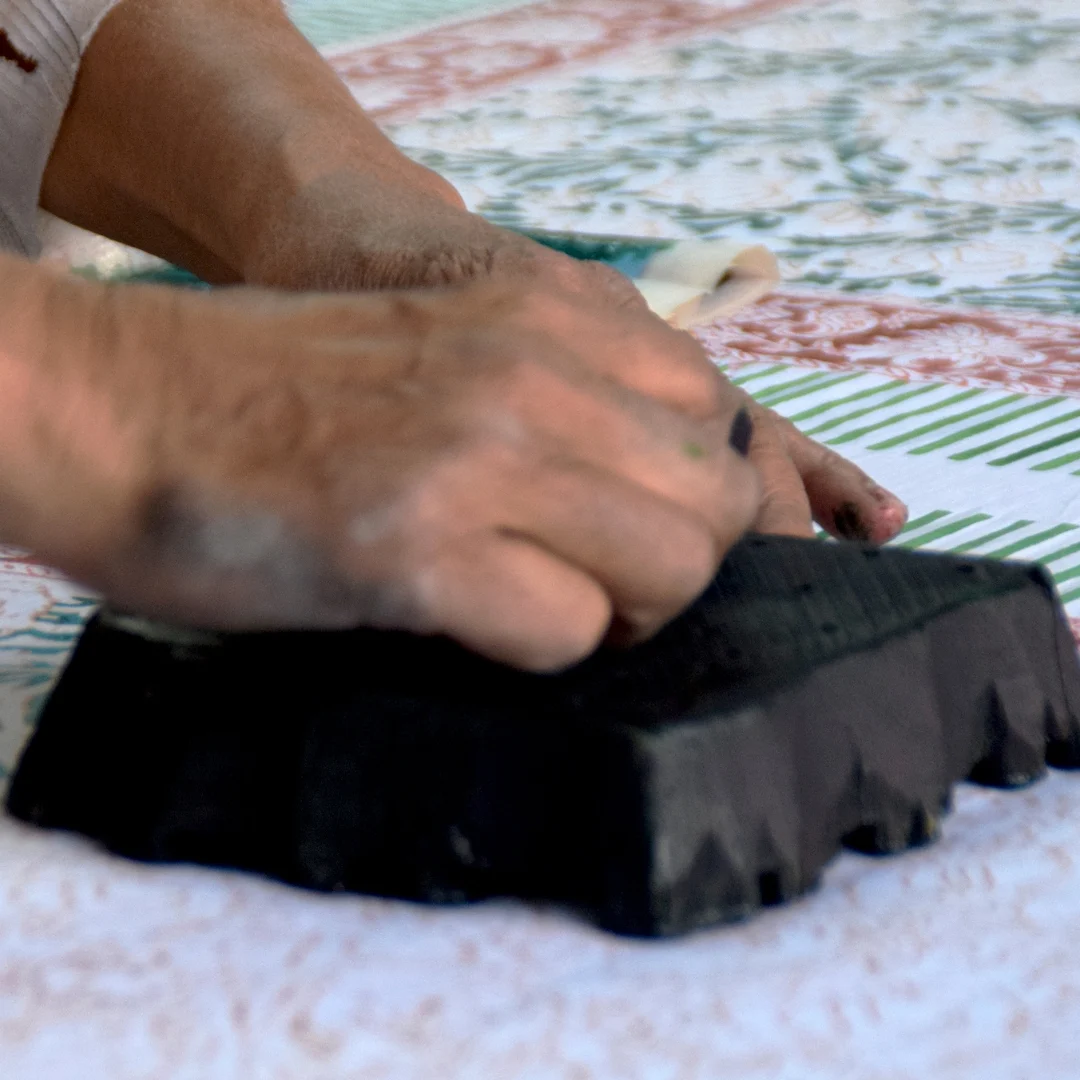 Close-up of hands pressing a wooden printing block onto fabric